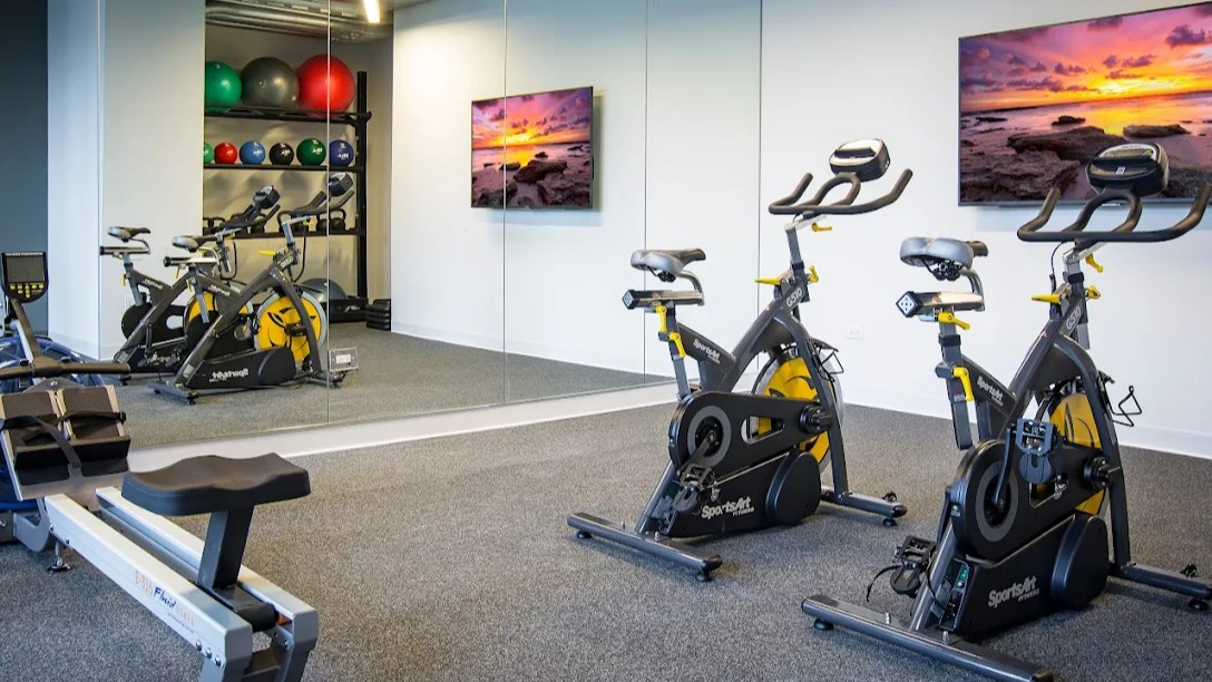 Dedicated fitness studio with spin bikes, a rowing machine, and weight storage, featuring large mirrors at Exhibit on Superior in Chicago