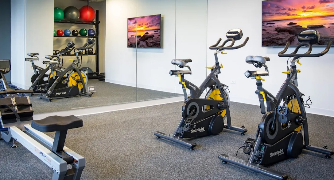 Dedicated fitness studio with spin bikes, a rowing machine, and weight storage, featuring large mirrors at Exhibit on Superior in Chicago