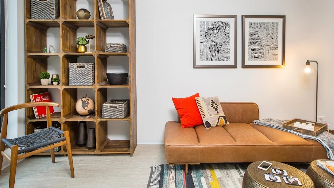 Modern living room with a brown chaise lounge, colorful rug, and a large wooden bookshelf at Exhibit on Superior apartments in Chicago