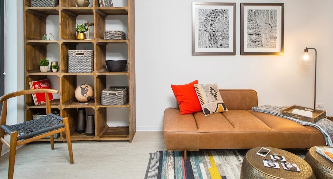 Modern living room with a brown chaise lounge, colorful rug, and a large wooden bookshelf at Exhibit on Superior apartments in Chicago