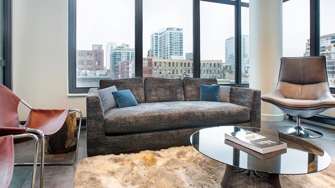 Chic living room with a comfortable sofa, unique chairs, and large windows offering urban city views at Exhibit on Superior in Chicago
