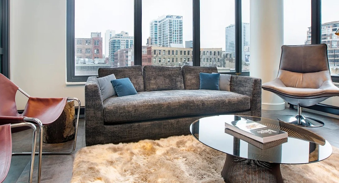 Chic living room with a comfortable sofa, unique chairs, and large windows offering urban city views at Exhibit on Superior in Chicago