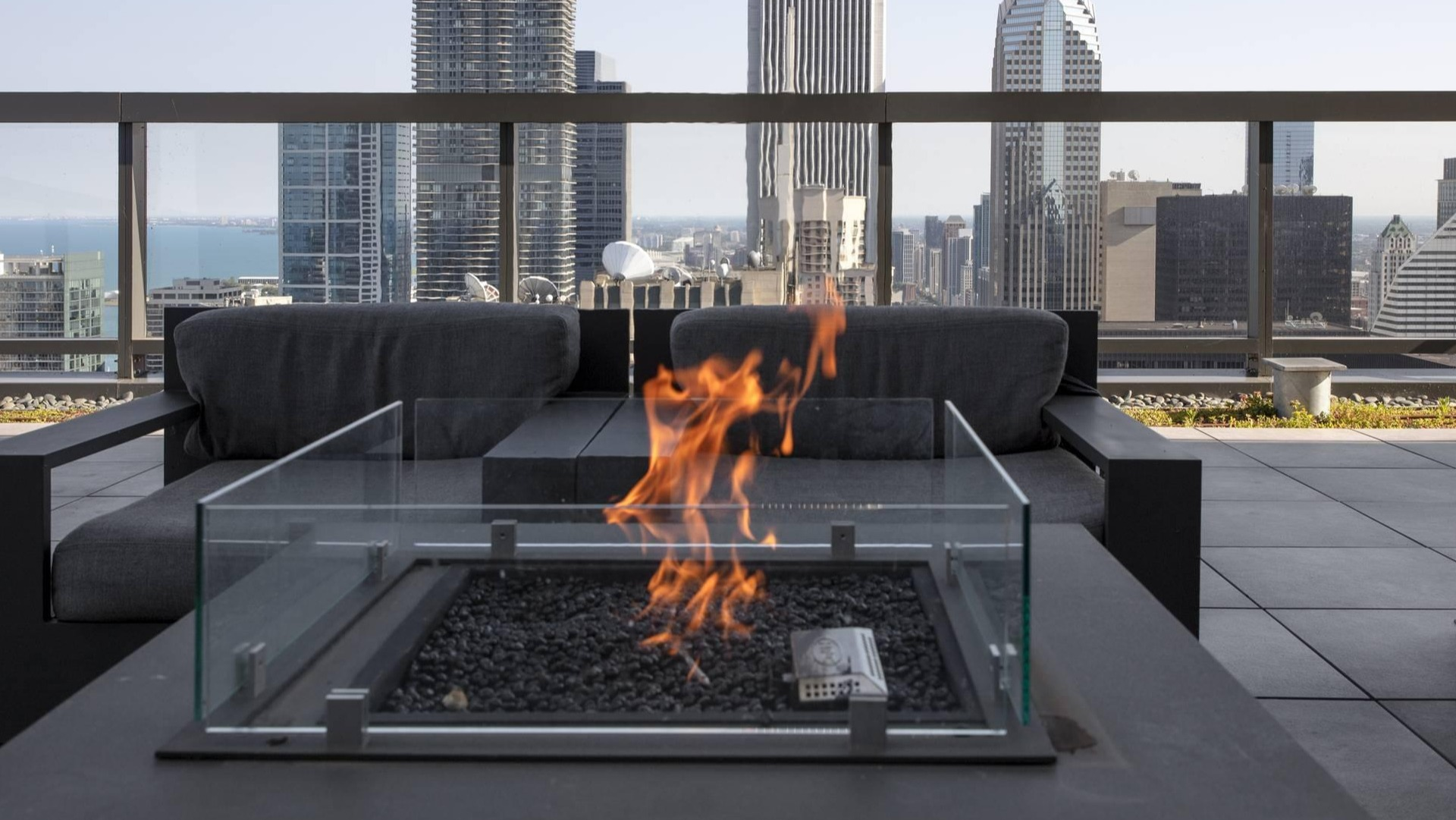 Rooftop terrace firepit with glass enclosure, modern lounge chairs, and Chicago skyline views at Optima Signature apartments