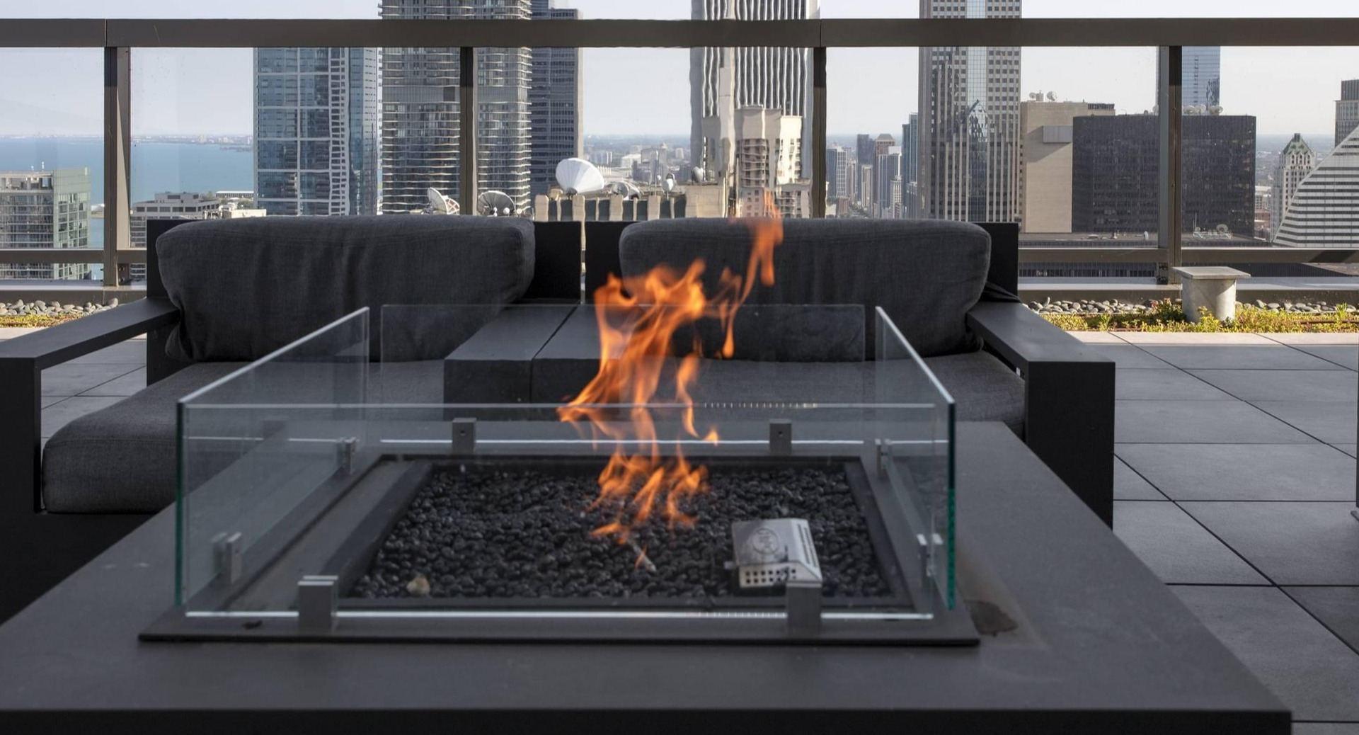 Rooftop terrace firepit with glass enclosure, modern lounge chairs, and Chicago skyline views at Optima Signature apartments
