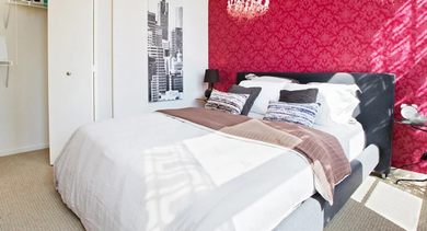 Chic apartment bedroom at Fisher Building Apartments in Chicago, featuring a bold red accent wall, elegant chandeliers, and ample closet space