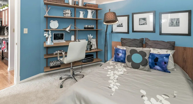 Cozy apartment bedroom at Fisher Building Apartments in Chicago, with a vibrant blue accent wall, comfortable bed, and a built-in desk area