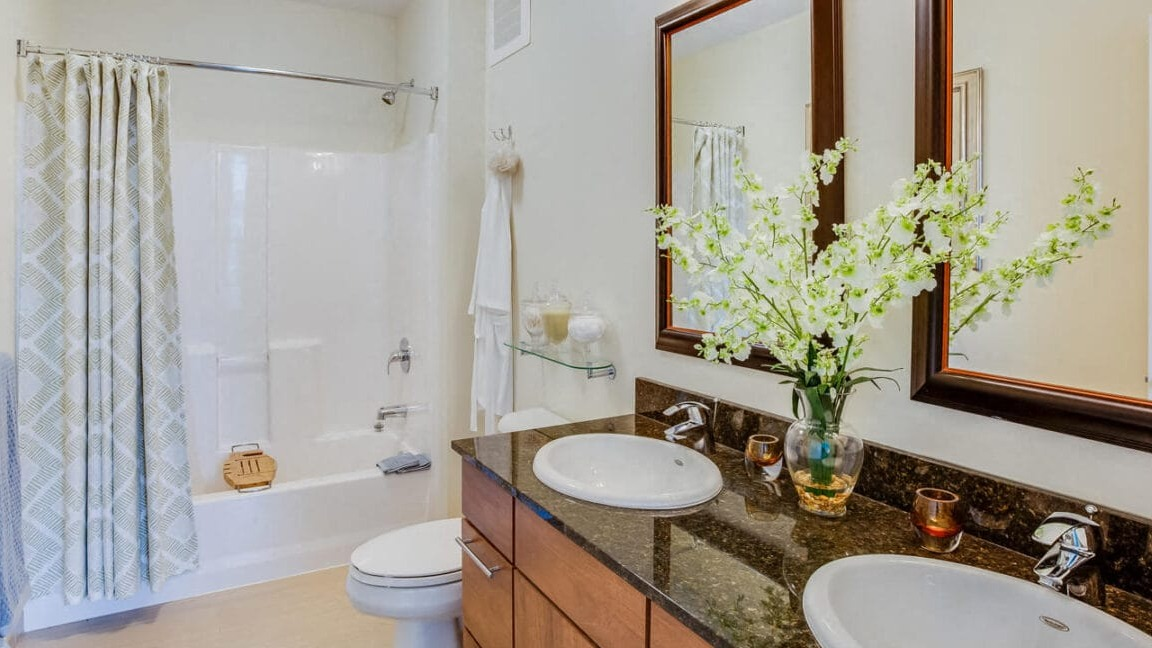 Spacious apartment bathroom at Flair Tower Apartments in Chicago, featuring a double vanity, large mirrors, and a shower-tub combo