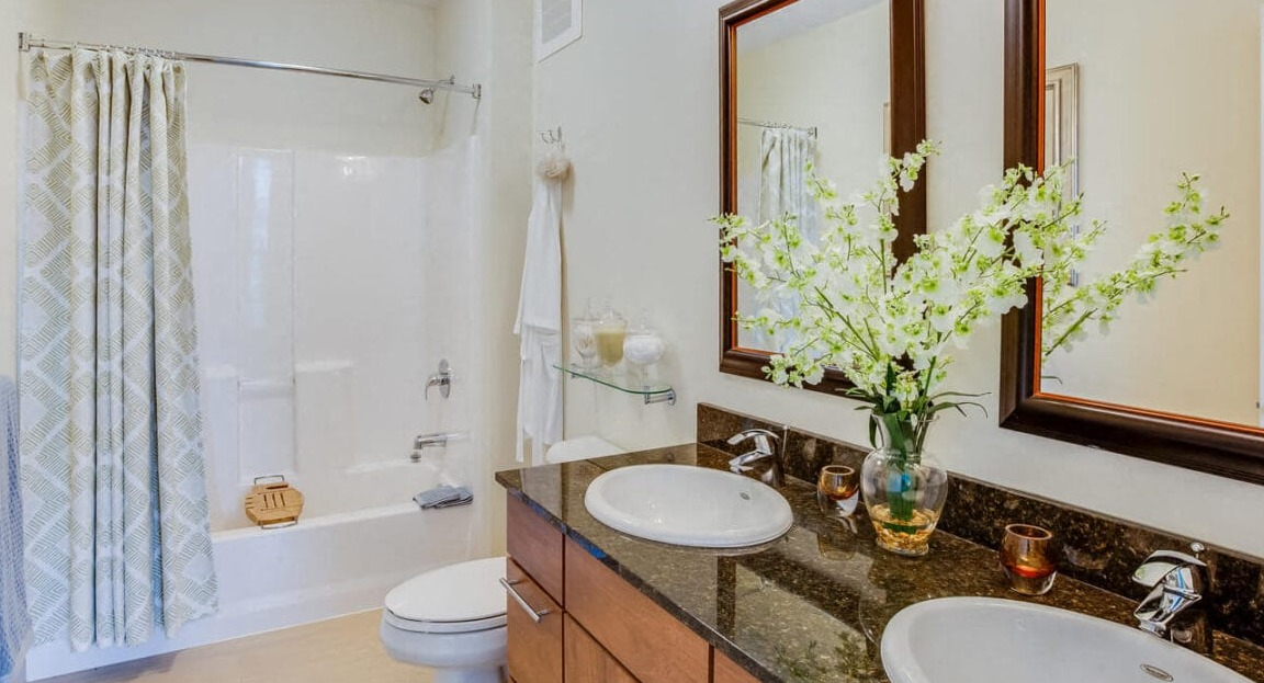Spacious apartment bathroom at Flair Tower Apartments in Chicago, featuring a double vanity, large mirrors, and a shower-tub combo