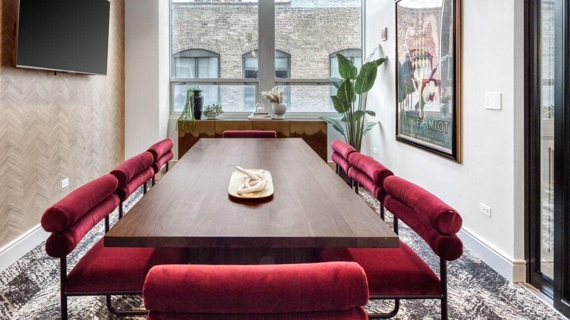 Stylish conference room at Flair Tower Apartments in Chicago, featuring a large wooden table, red velvet seating, and modern lighting
