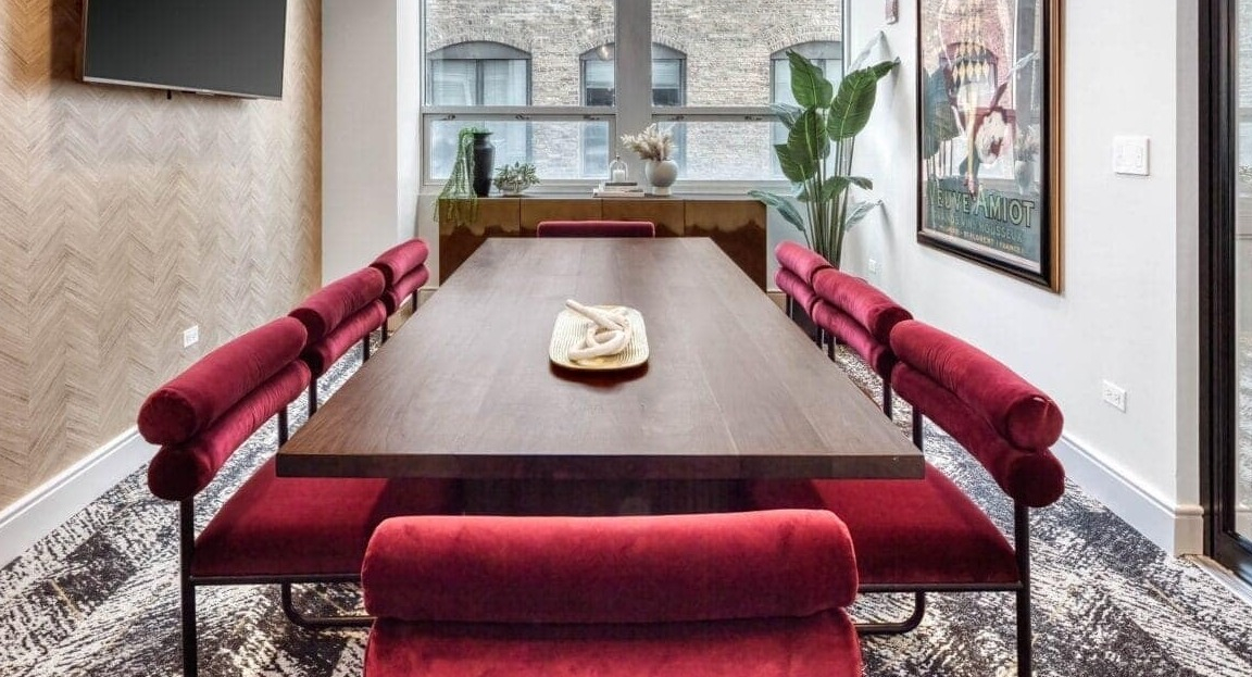Stylish conference room at Flair Tower Apartments in Chicago, featuring a large wooden table, red velvet seating, and modern lighting