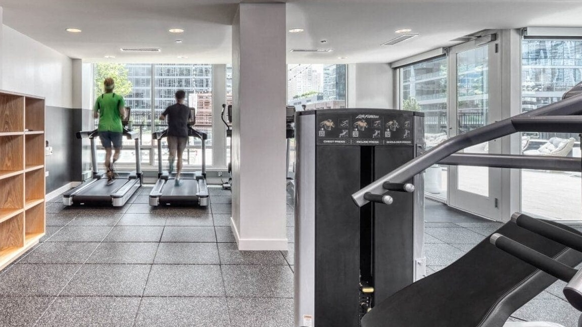 Modern fitness center at Flair Tower Apartments in Chicago, with treadmills and weight machines, offering city views through large windows