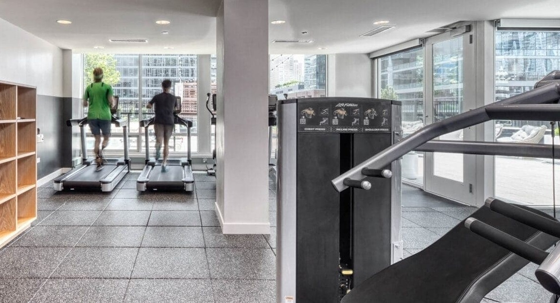 Modern fitness center at Flair Tower Apartments in Chicago, with treadmills and weight machines, offering city views through large windows