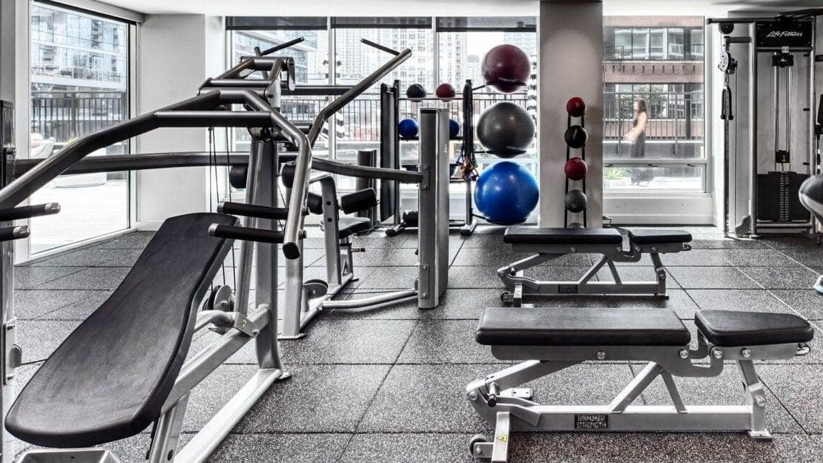 Spacious gym at Flair Tower Apartments in Chicago, equipped with various strength training machines, free weights, and fitness accessories
