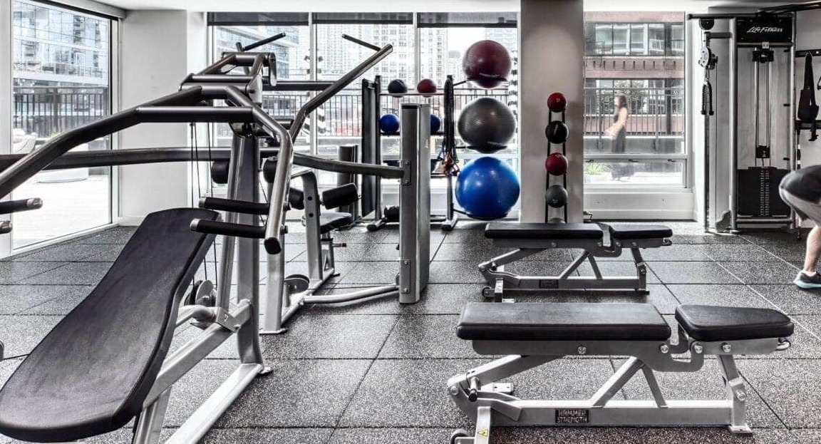 Spacious gym at Flair Tower Apartments in Chicago, equipped with various strength training machines, free weights, and fitness accessories