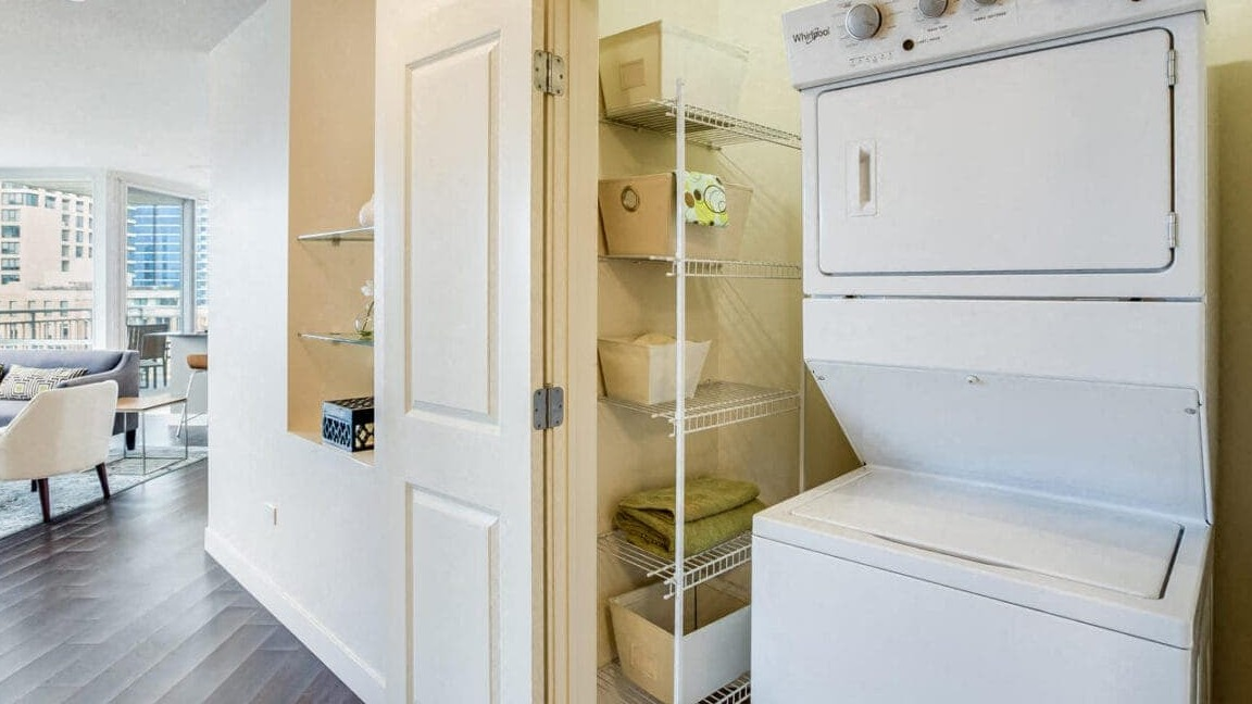 Convenient in-unit stacked washer and dryer with shelving in a hallway closet at Flair Tower Apartments in Chicago