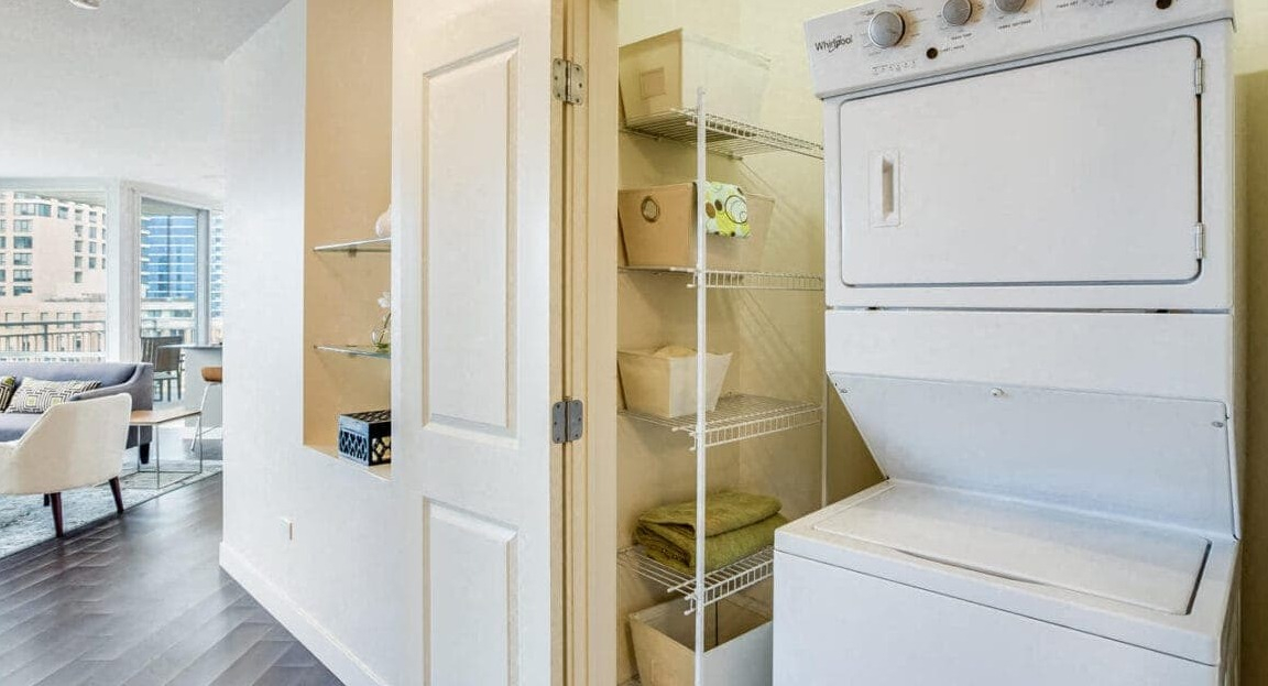 Convenient in-unit stacked washer and dryer with shelving in a hallway closet at Flair Tower Apartments in Chicago