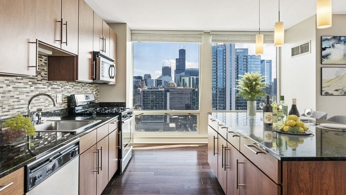 Gourmet apartment kitchen at Flair Tower Apartments in Chicago, with dark countertops, wood cabinetry, and stunning city skyline views from the window