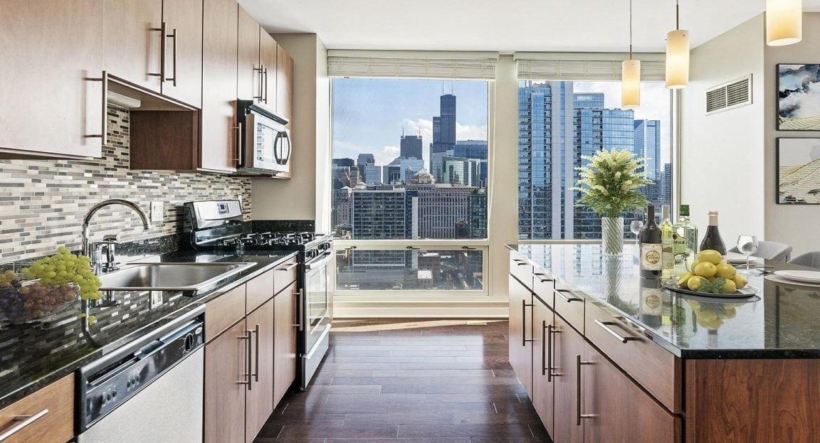 Gourmet apartment kitchen at Flair Tower Apartments in Chicago, with dark countertops, wood cabinetry, and stunning city skyline views from the window