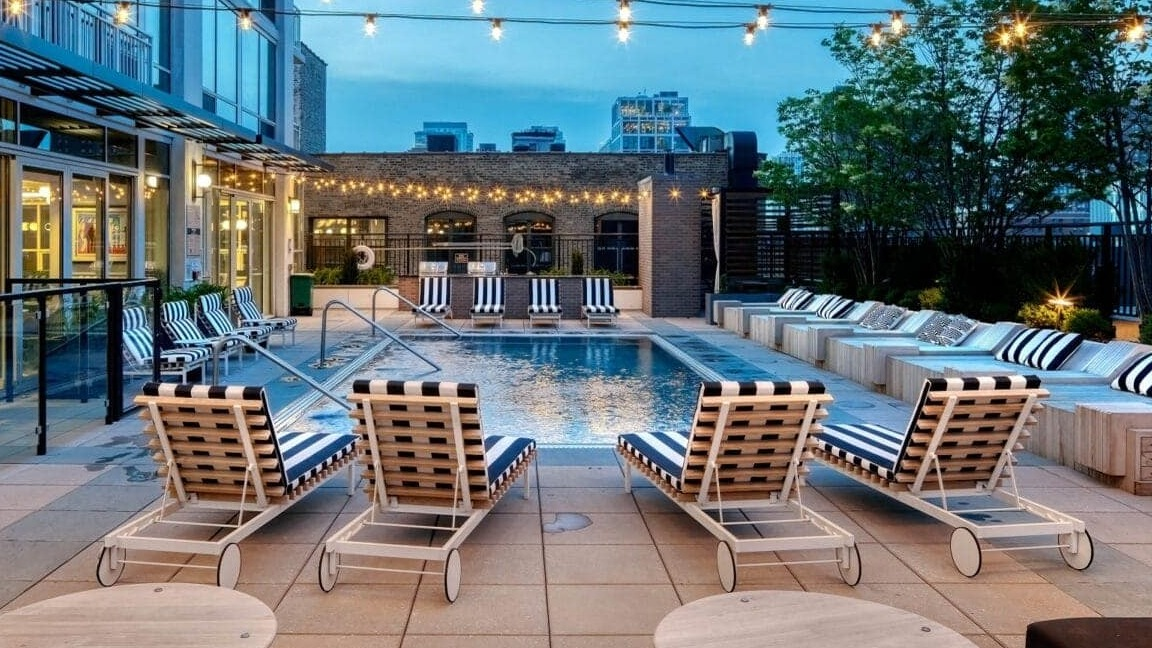 Evening view of the outdoor pool deck at Flair Tower Apartments in Chicago, illuminated by string lights, with comfortable seating