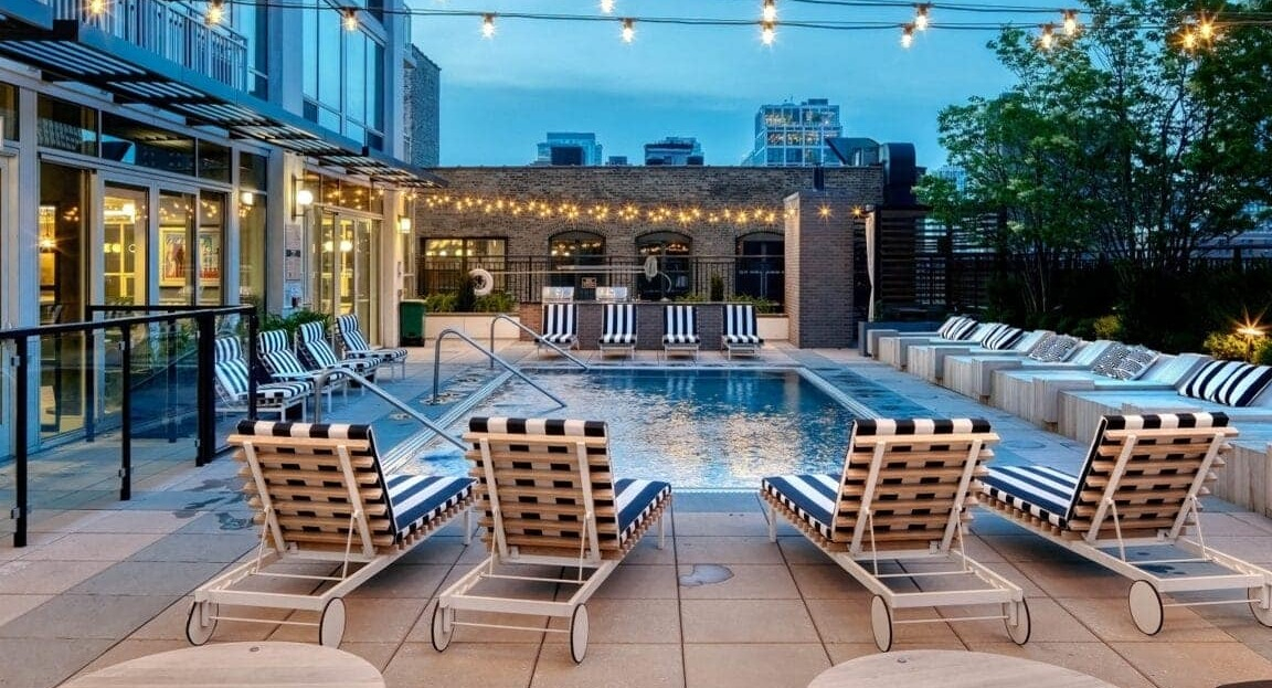 Evening view of the outdoor pool deck at Flair Tower Apartments in Chicago, illuminated by string lights, with comfortable seating