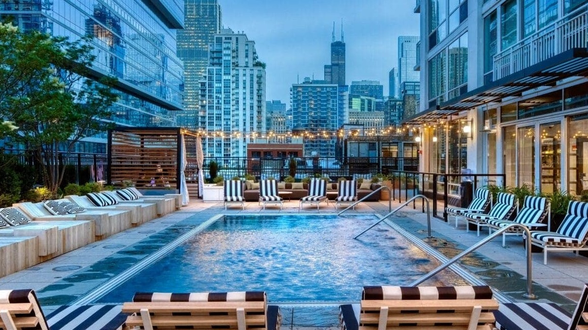 Vibrant outdoor pool deck at Flair Tower Apartments in Chicago, featuring a sparkling pool, lounge seating, and stunning city skyline views