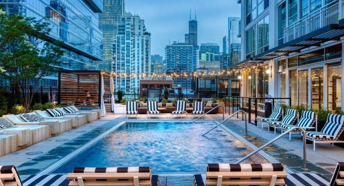 Vibrant outdoor pool deck at Flair Tower Apartments in Chicago, featuring a sparkling pool, lounge seating, and stunning city skyline views