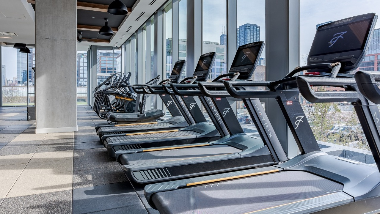 Bright cardio fitness center at Flora apartments in Chicago, featuring treadmills with city views through large windows