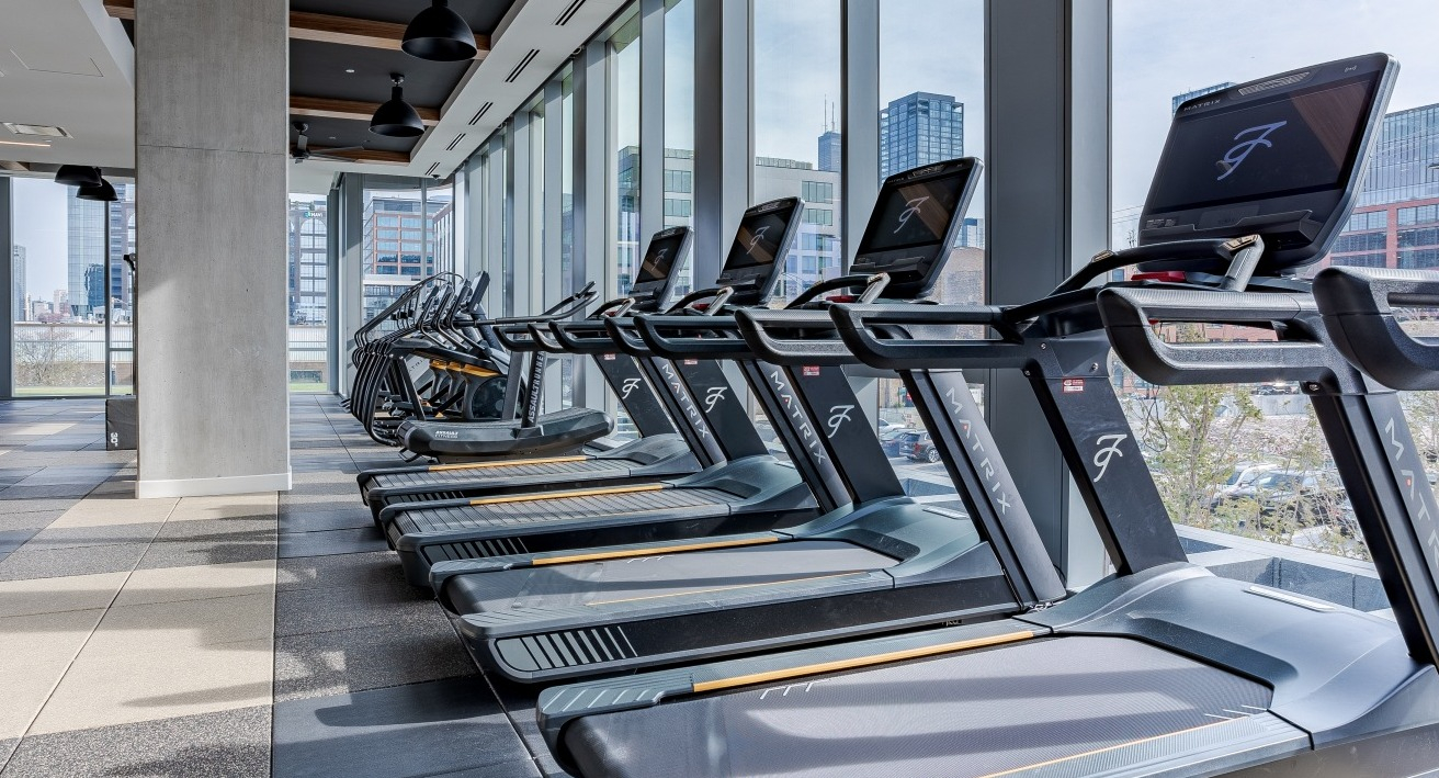 Bright cardio fitness center at Flora apartments in Chicago, featuring treadmills with city views through large windows