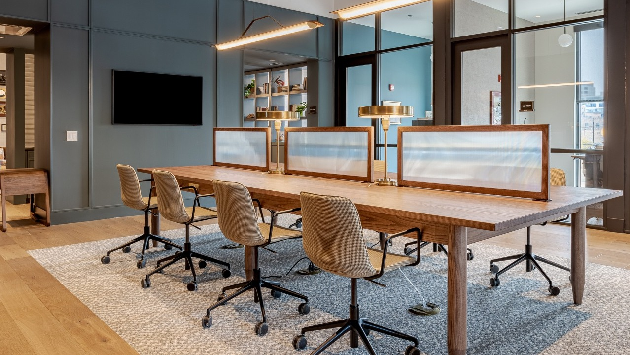 Stylish co-working space at Flora apartments in Chicago, featuring a long communal desk, ergonomic chairs, and modern lighting for productivity