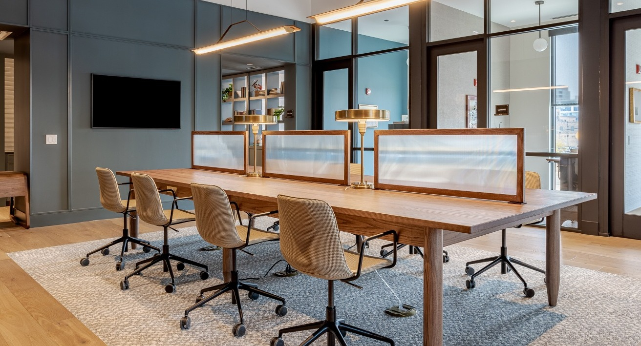 Stylish co-working space at Flora apartments in Chicago, featuring a long communal desk, ergonomic chairs, and modern lighting for productivity