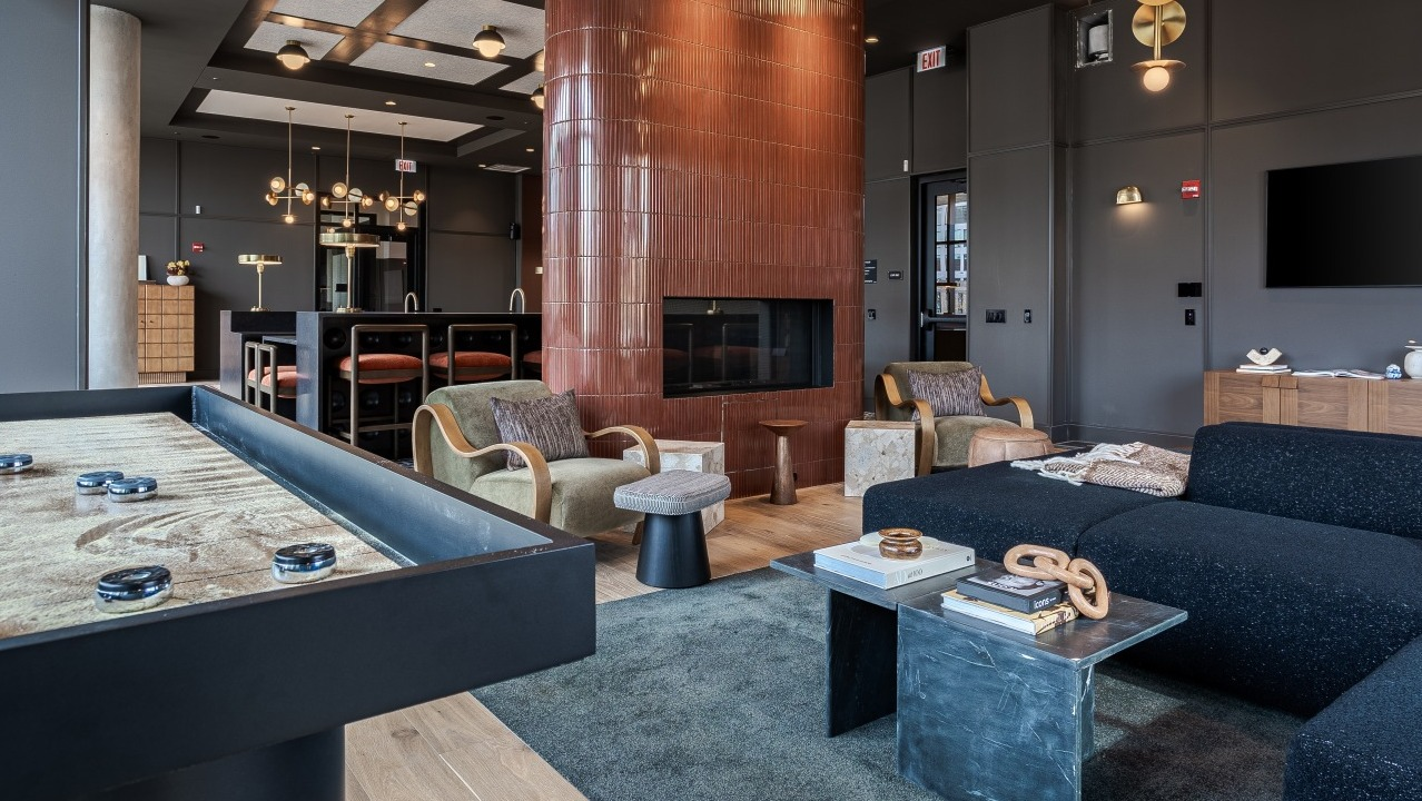Lively game room and lounge area at Flora apartments in Chicago, featuring a shuffleboard table, cozy seating, and a modern fireplace