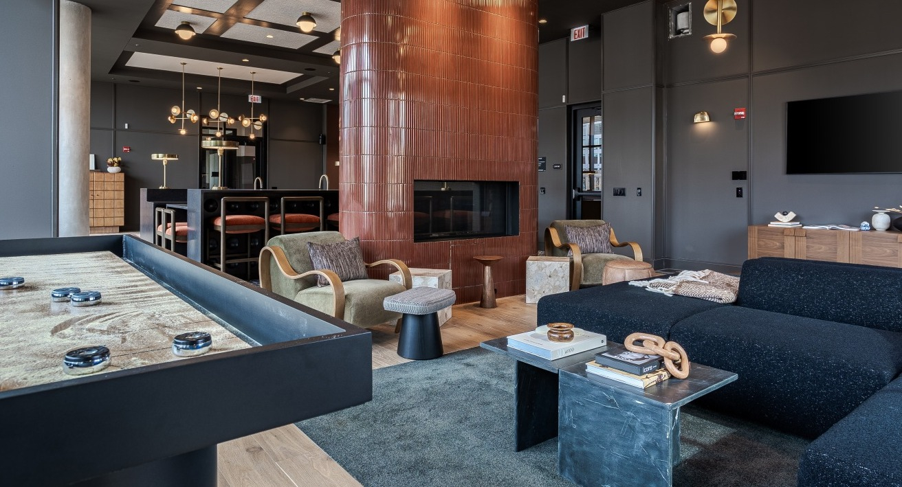 Lively game room and lounge area at Flora apartments in Chicago, featuring a shuffleboard table, cozy seating, and a modern fireplace