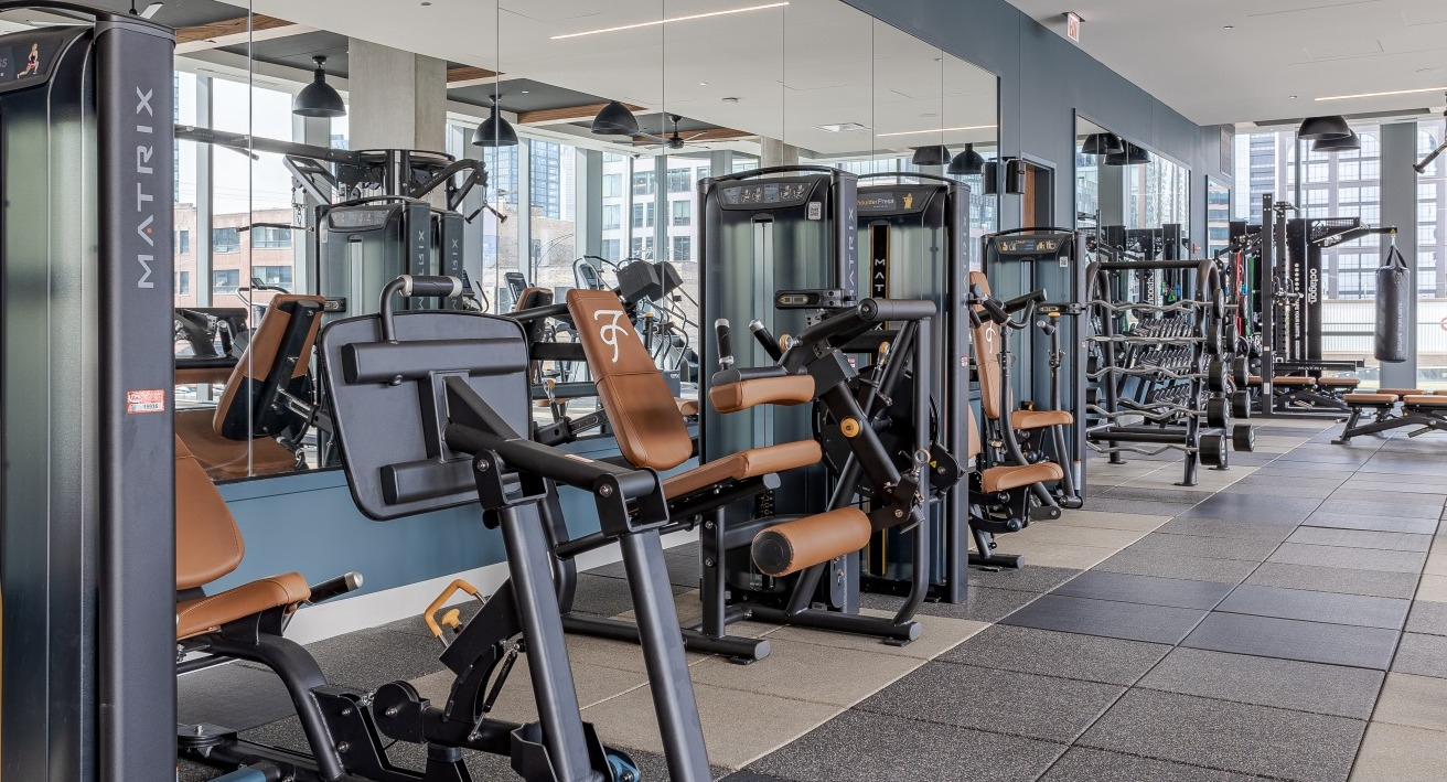 Modern gym at Flora apartments in Chicago, equipped with various strength training machines and mirrors, perfect for a full workout