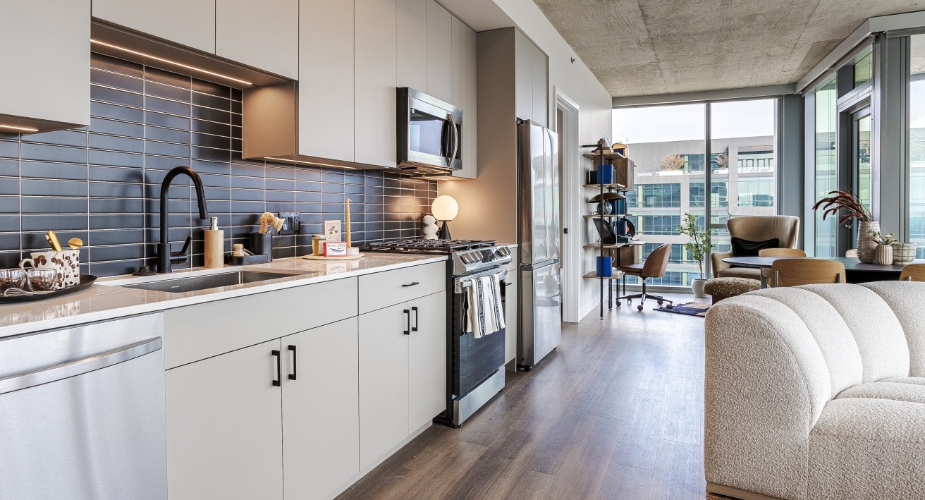 Bright apartment kitchen at Flora in Chicago, featuring light cabinetry, a dark subway tile backsplash, and an open view into the living space