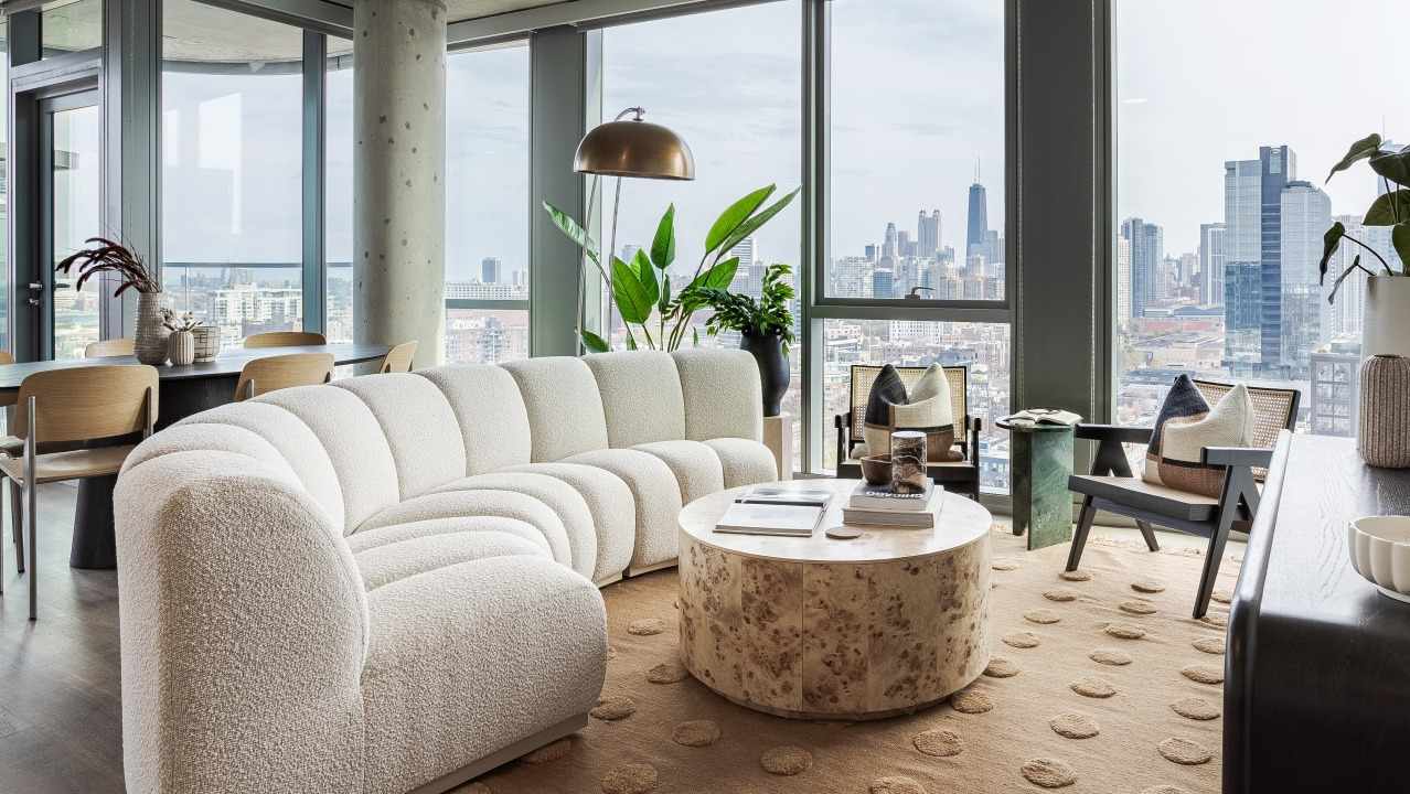 Spacious apartment living room at Flora in Chicago, with a large curved sofa, elegant decor, and expansive windows offering panoramic city views