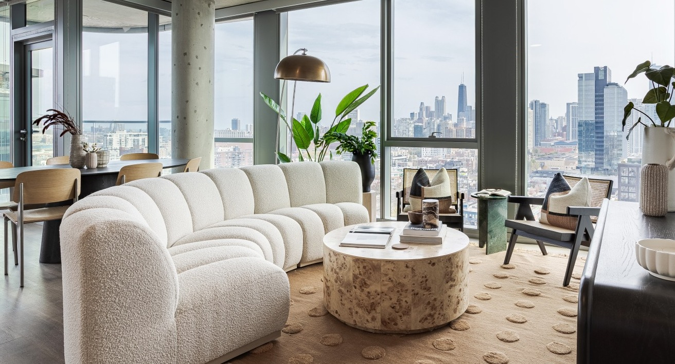 Spacious apartment living room at Flora in Chicago, with a large curved sofa, elegant decor, and expansive windows offering panoramic city views