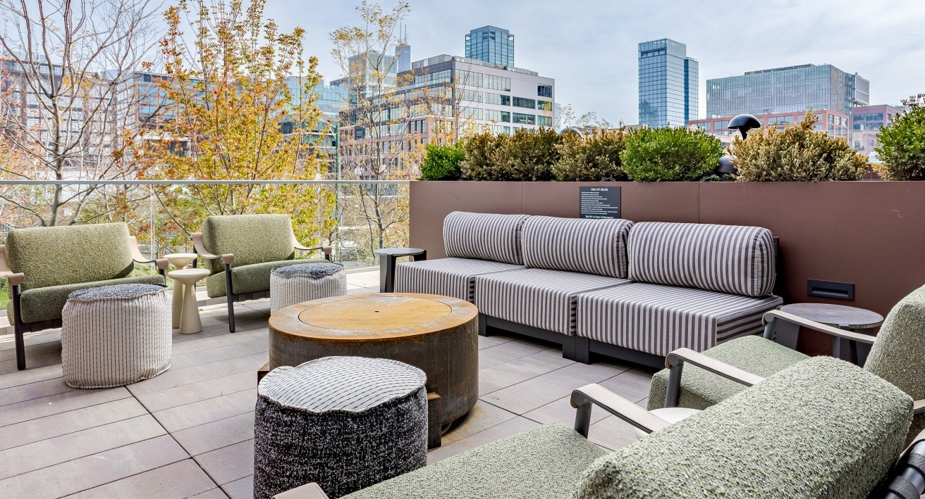 Inviting outdoor patio lounge at Flora apartments in Chicago, with comfortable seating, lush greenery, and stunning city views