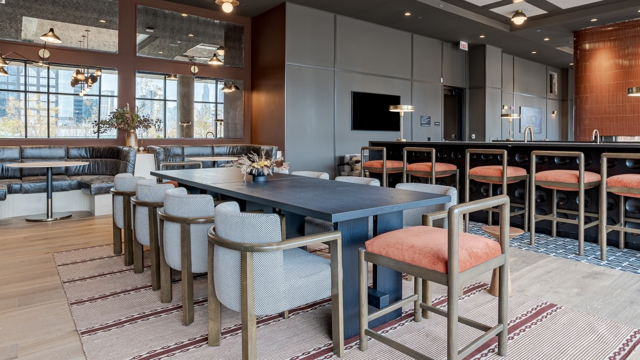 Elegant resident lounge and dining space at Flora apartments in Chicago, with a large communal table, bar seating, and a modern fireplace