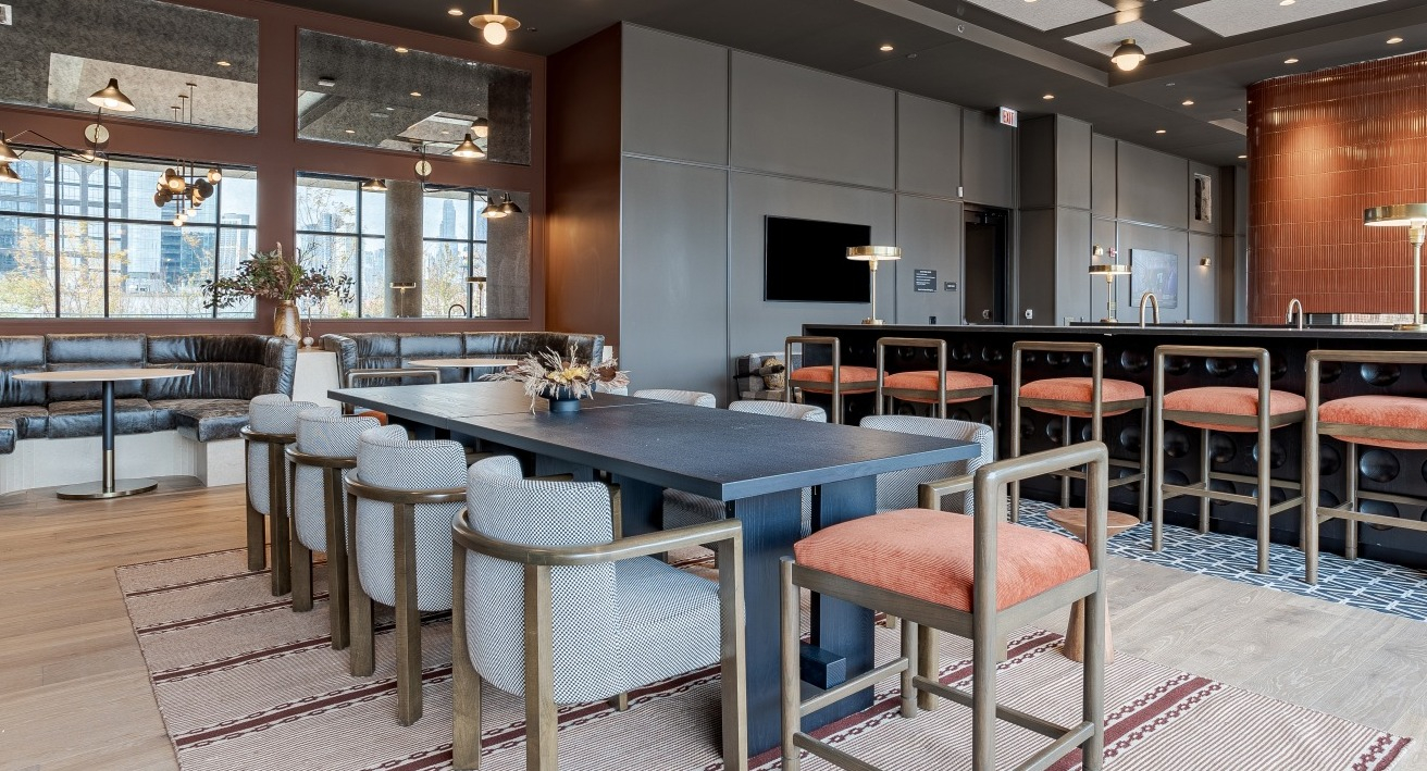 Elegant resident lounge and dining space at Flora apartments in Chicago, with a large communal table, bar seating, and a modern fireplace