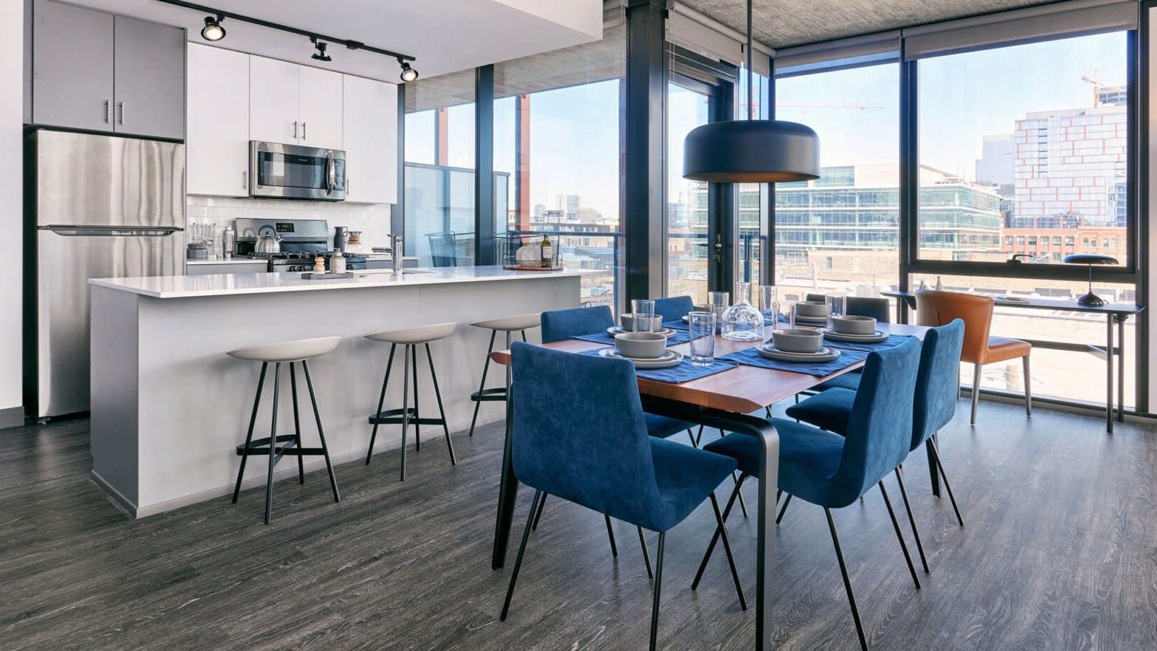Contemporary apartment kitchen and dining area at Fulbrix Apartments in Chicago, featuring a breakfast bar, blue dining chairs, and city views