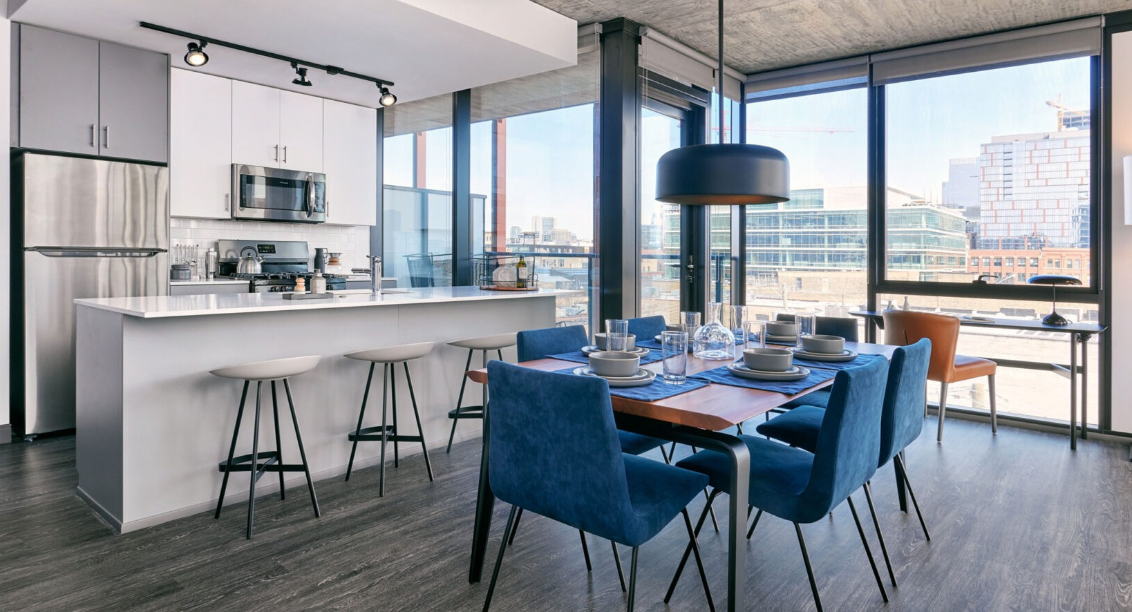 Contemporary apartment kitchen and dining area at Fulbrix Apartments in Chicago, featuring a breakfast bar, blue dining chairs, and city views