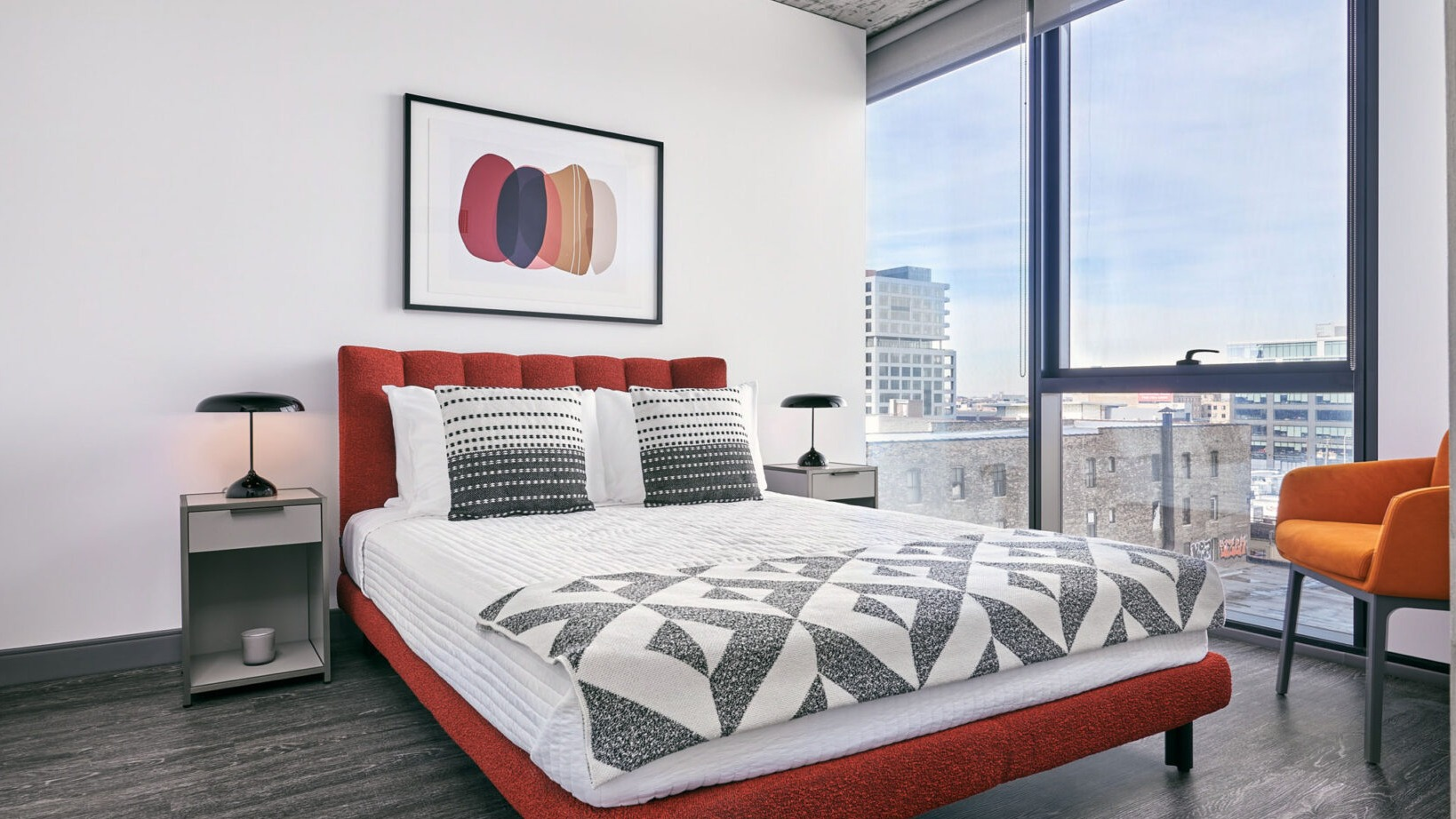 Stylish apartment bedroom at Fulbrix Apartments in Chicago, featuring a red upholstered bed, patterned bedding, and large windows with city views