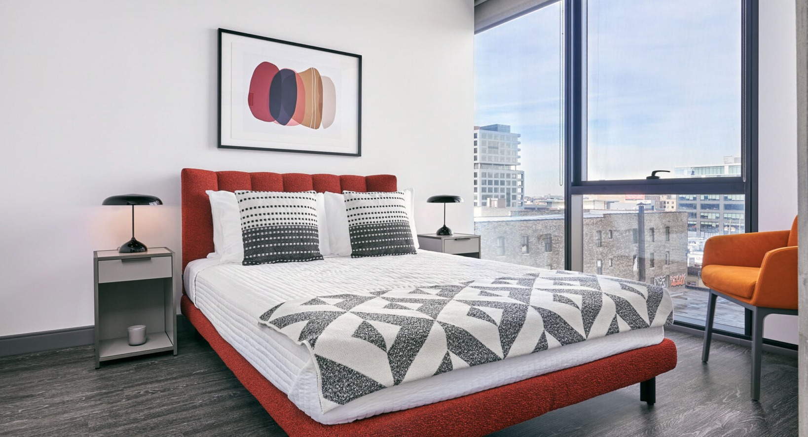 Stylish apartment bedroom at Fulbrix Apartments in Chicago, featuring a red upholstered bed, patterned bedding, and large windows with city views