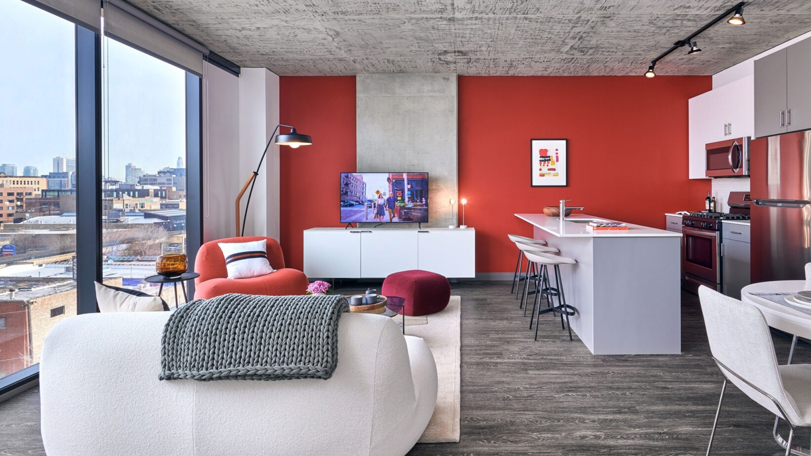 Modern open-concept living and kitchen area at Fulbrix Apartments in Chicago, featuring a red accent wall, stylish furniture, and city views