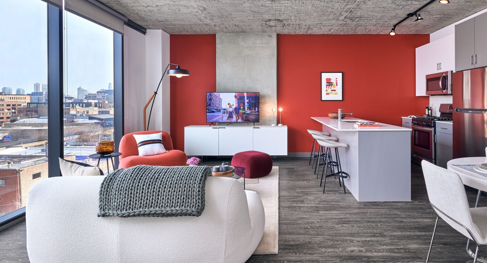 Modern open-concept living and kitchen area at Fulbrix Apartments in Chicago, featuring a red accent wall, stylish furniture, and city views