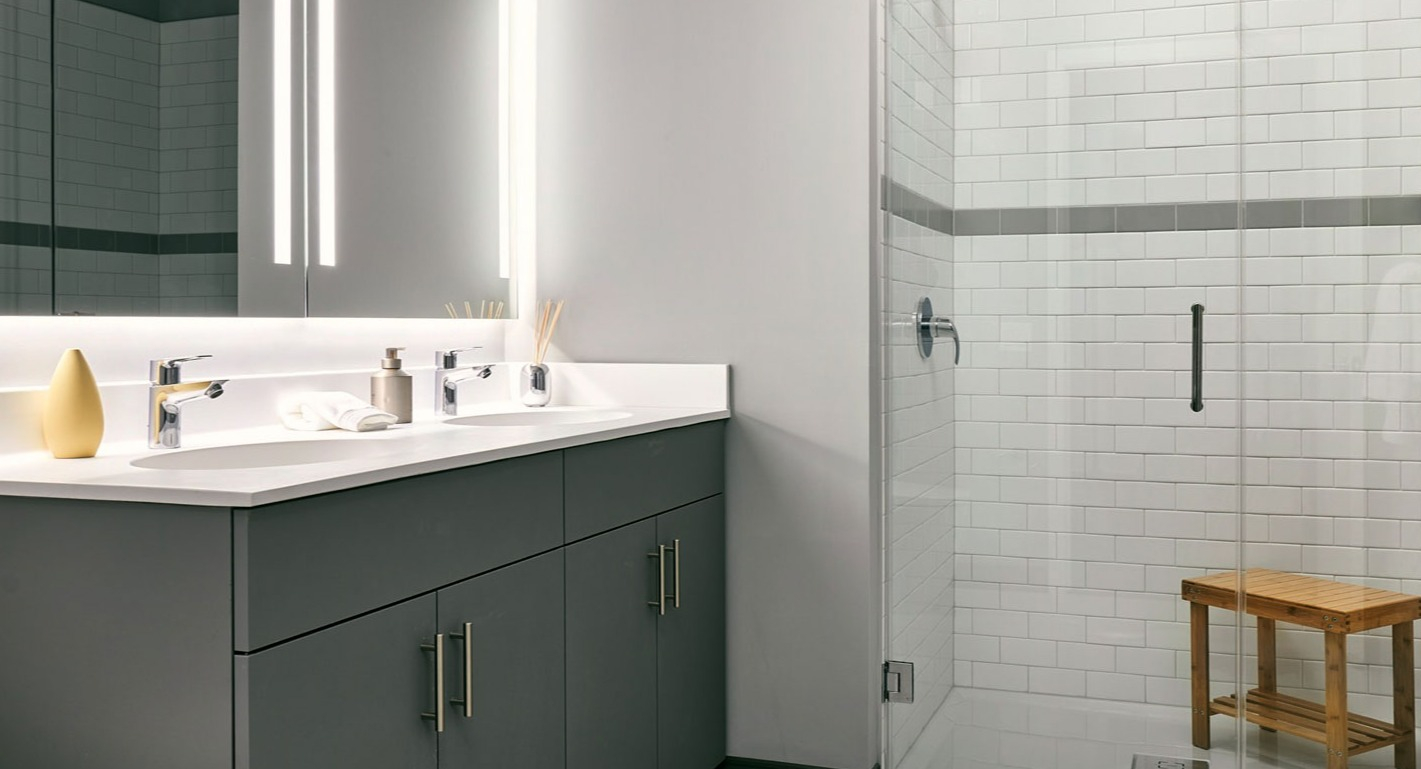 Spacious apartment bathroom at Fulbrix Apartments in Chicago, featuring a double vanity, large illuminated mirror, and a glass walk-in shower