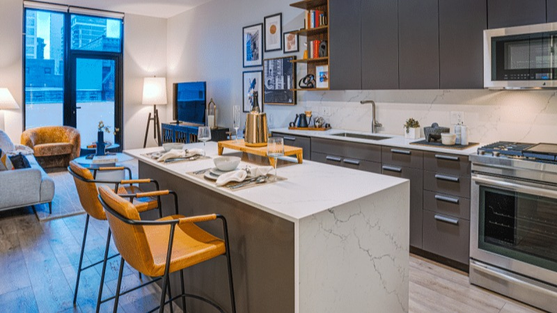 Open-concept kitchen and living area with a large island, stylish furniture, and bright windows at Gild apartments in Chicago