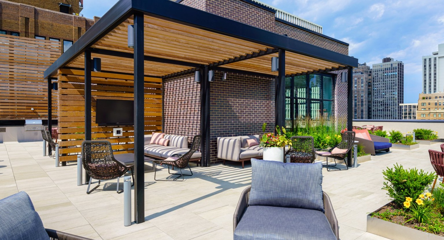 Stylish rooftop lounge area featuring a shaded pergola, comfortable seating, and outdoor TVs at Gild apartments in Chicago