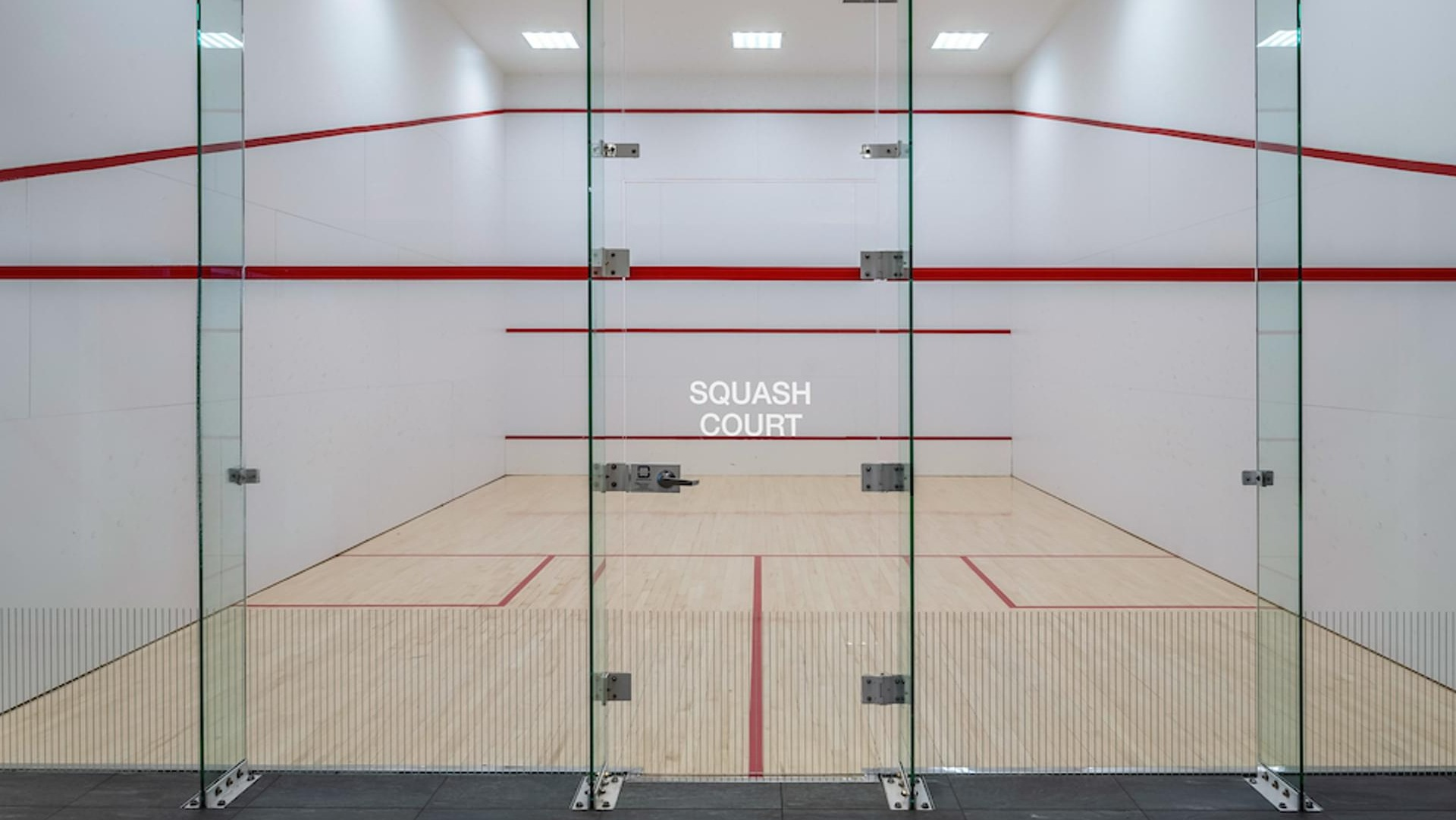 Professional glass-walled squash court with hardwood floors and red boundary lines at Optima Signature apartments in Chicago