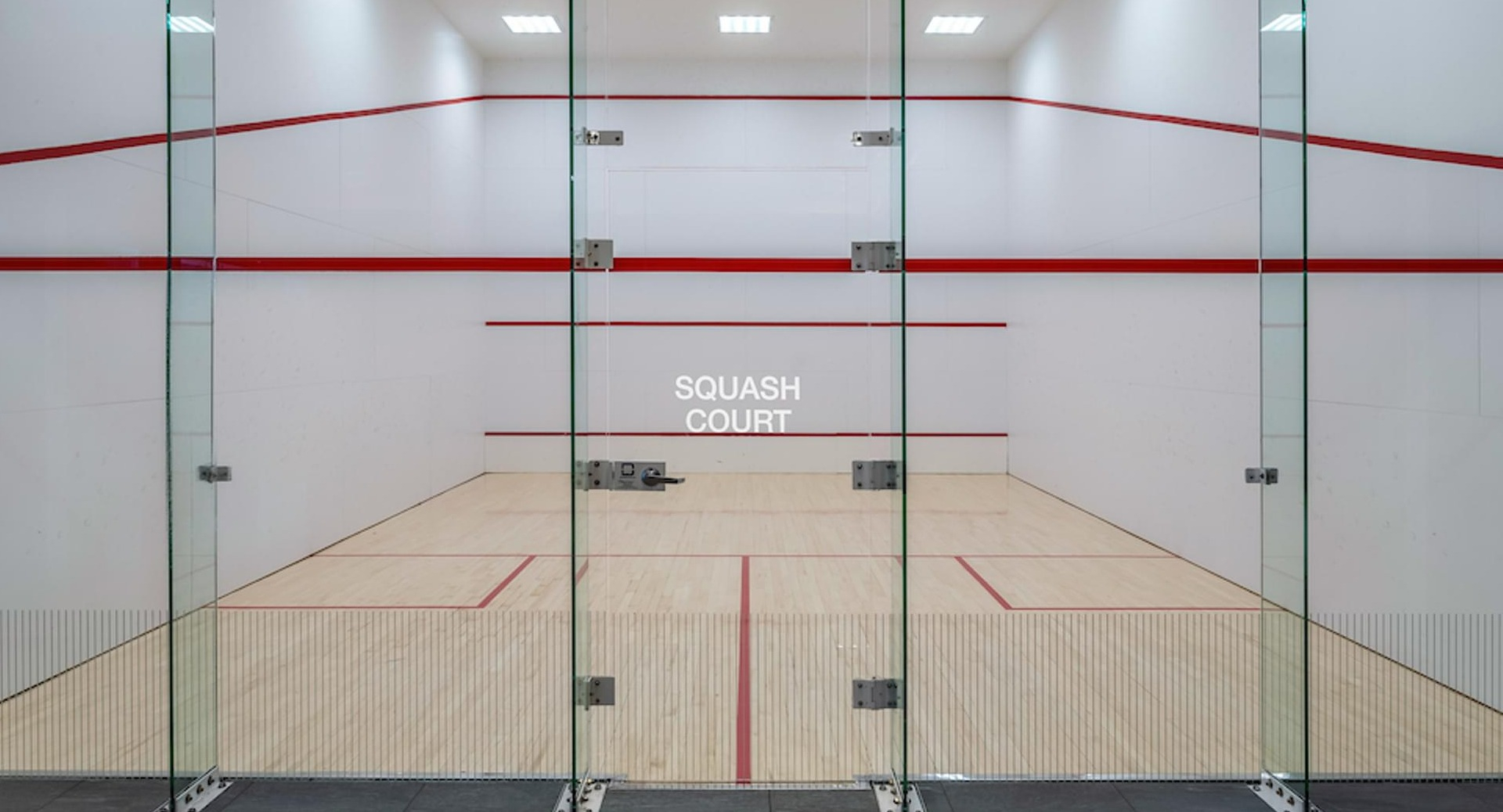 Professional glass-walled squash court with hardwood floors and red boundary lines at Optima Signature apartments in Chicago
